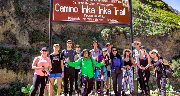 Groupe de randonneurs posant sous un grand panneau du sentier Camino Inka au point de départ, avec des bâtons de trekking