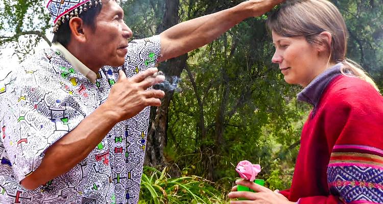 Un chamán indígena realiza un ritual de limpieza con humo sobre un visitante que sostiene una flor en el Amazonas