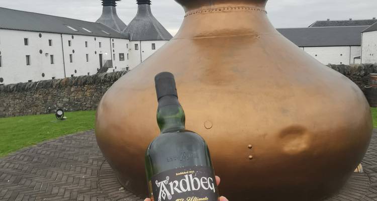 Large copper distillery pot with a hand holding a whiskey bottle in front.