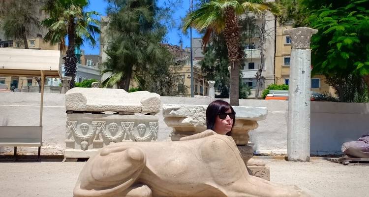 Woman posing beside a lion statue at an archaeological site.