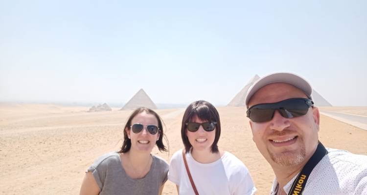 Three people taking a selfie with the Pyramids of Giza in the background.