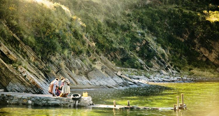 Tres personas de pie en un muelle junto a un río pintoresco con acantilados empinados.