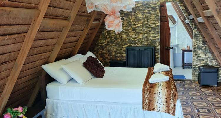 Gemütliches Inneres eines Bungalows mit Reetdach mit Doppelbett, Moskitonetz und rustikaler Steinwanddekorationen