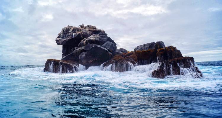 Rocky island surrounded by waves in an ocean.