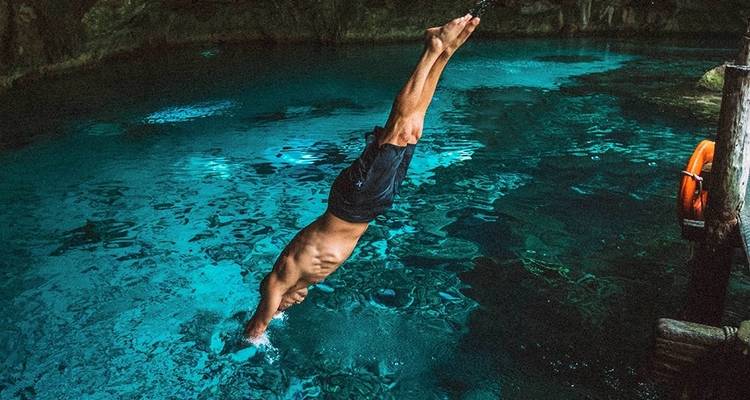 Un homme plongeant avec grâce dans une eau bleu cristallin à l'intérieur d'un cenote naturel