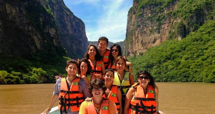 Groupe d'amis portant des gilets de sauvetage souriants à bord d'un bateau naviguant dans un canyon verdoyant aux parois abruptes
