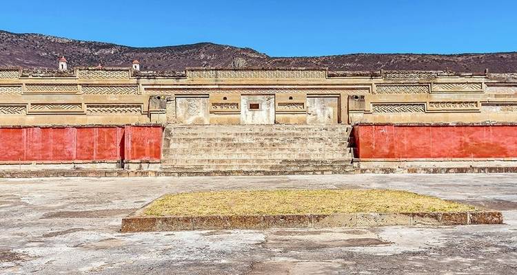 Vaste cour et façades de pierre complexes du site archéologique de Mitla sous un ciel dégagé.