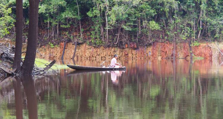 Persona en una canoa de madera navegando por un río tranquilo rodeado de exuberante vegetación.