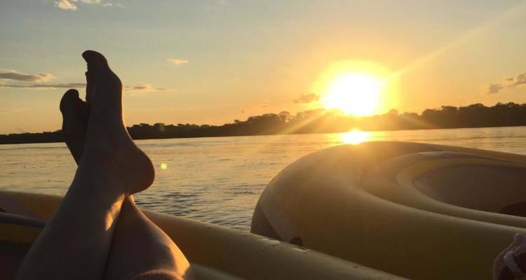 Escena relajante de piernas descansando en un bote durante la puesta de sol en un río.