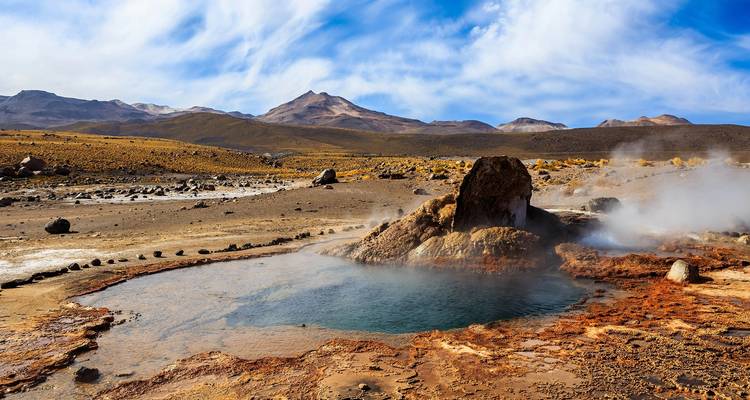 Geothermisch gebied met warme bronnen die stoom uitstoten in een bergachtig landschap.