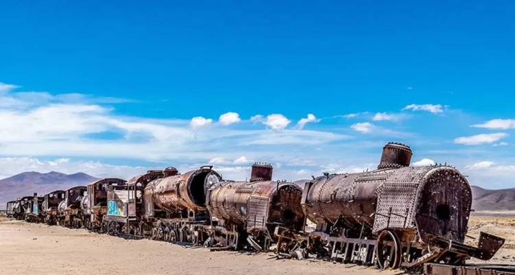 Trenes oxidados y abandonados en un paisaje desértico bajo un cielo azul claro.