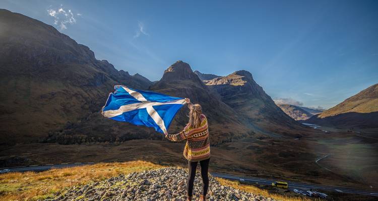 Woman holding Scottish flag in a mountainous landscape.
