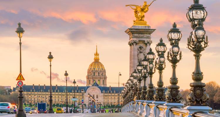 Pont Alexandre III avec Les Invalides illuminés au coucher du soleil.