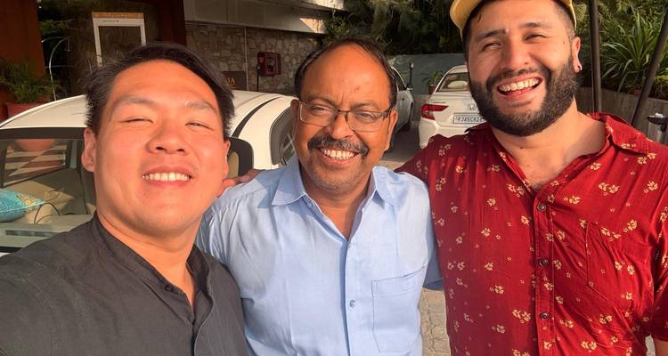 Three smiling people posing in front of cars.