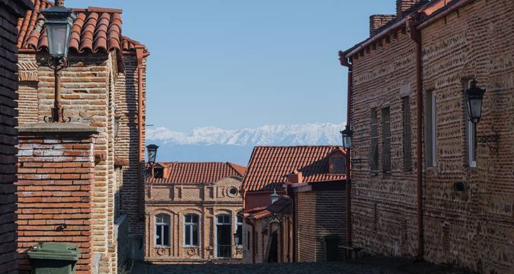 Narrow street with historic buildings and distant mountains.