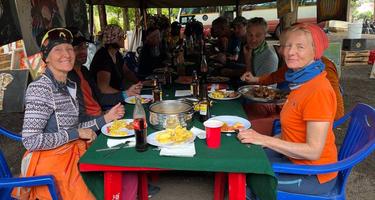 Trekker teilen eine herzhafte Mahlzeit in einem Campingplatz-Speisezelt mit Tellern voller Pommes und Getränken.