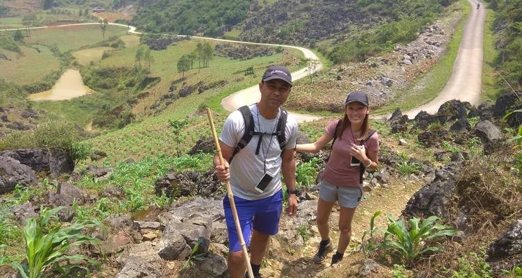 Zwei Wanderer mit einem Wanderstock auf einem steinigen Bergpfad mit Blick auf kultivierte Täler
