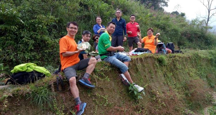 Gruppe von Wanderern, die auf einem grasbewachsenen Hang sitzen und während einer Wanderung Snacks genießen