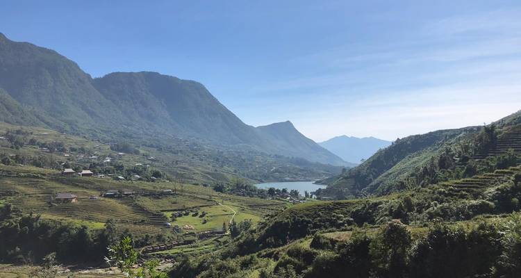 Bassin montagneux avec un petit lac, des fermes éparpillées et des collines en terrasses sous un ciel bleu dégagé