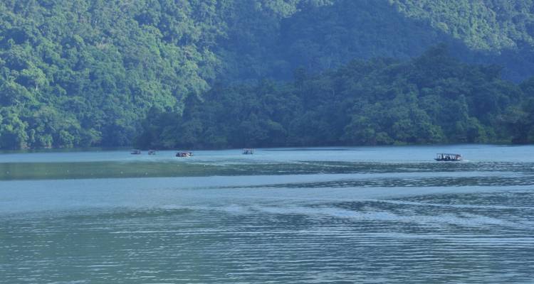 Pequeñas lanchas motoras salpicando un amplio lago bordeado por un denso bosque y altos acantilados