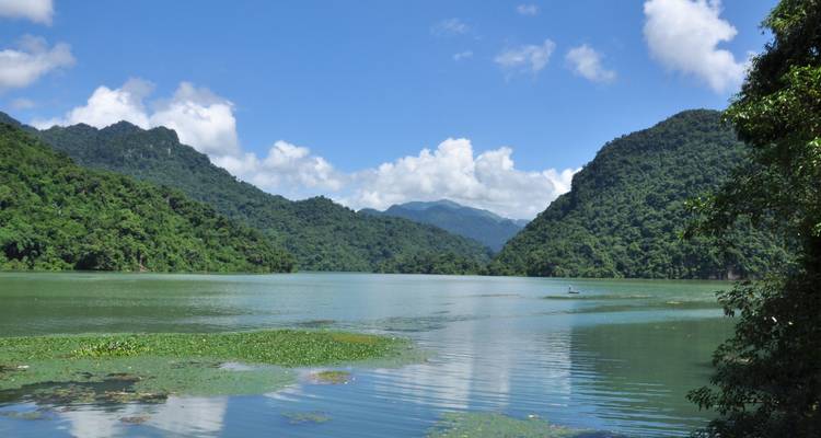 Vista serena del lago Ba Be rodeado de exuberantes montañas verdes bajo un cielo azul despejado.