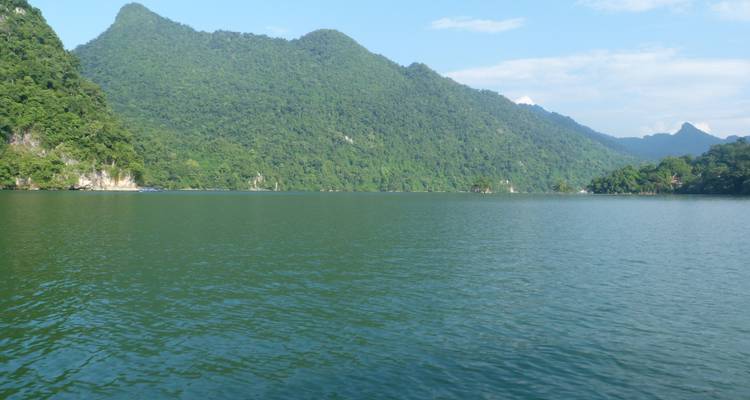 Amplias colinas cubiertas de verde reflejadas en un tranquilo lago azul bajo un cielo despejado