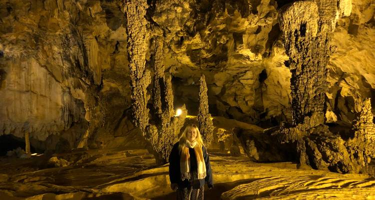 Visitor standing inside an illuminated limestone cave with tall stalagmites