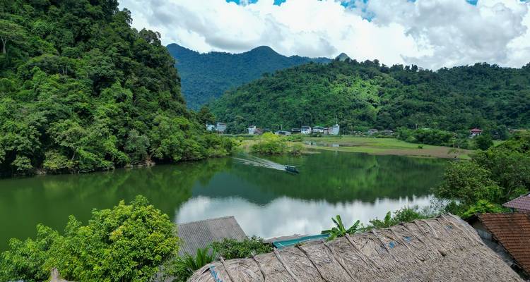 Green hills and rainforest reflect on a placid river with a longboat wake cutting across.