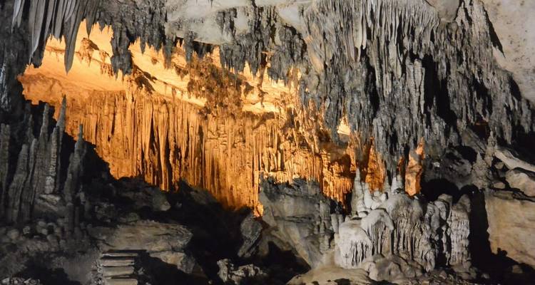 Illuminated limestone formations and stalactites inside a large cave chamber