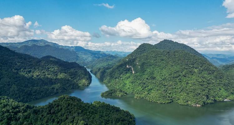 High aerial view of a winding green river through dense mountain jungle under blue skies.
