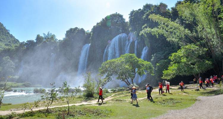 Visitors walk a riverside path with powerful multi-tiered waterfalls and spray in the background.