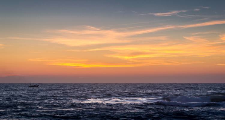 A serene ocean view at sunset with waves and a distant boat.