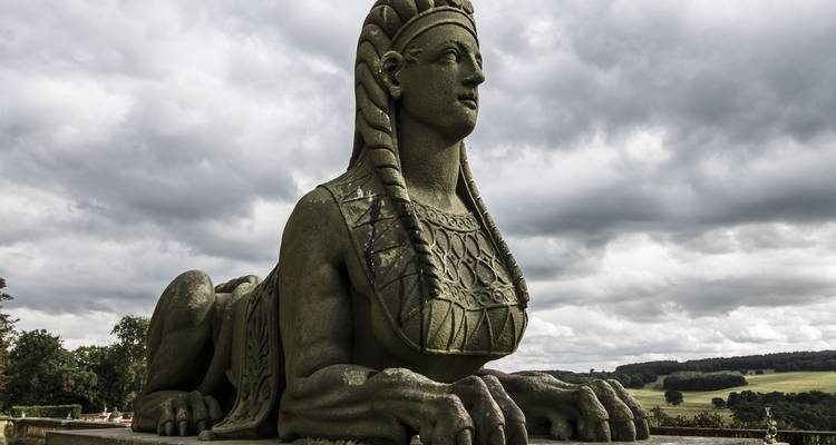 A stone statue in an open landscape with a cloudy sky.