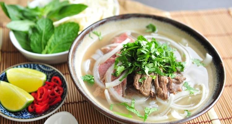 Bowl of Vietnamese pho with herbs and ingredients.