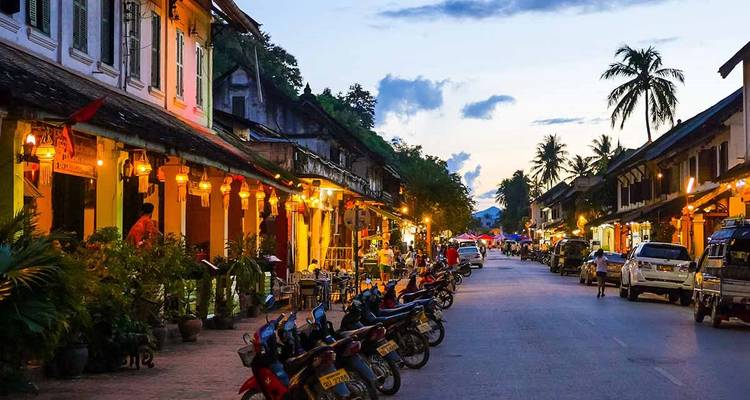 Evening scene of Luang Prabang’s main street lined with French-colonial buildings, glowing lanterns and parked motorbikes.