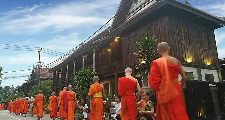 Morning alms procession with lines of saffron-robed Buddhist monks walking past wooden houses in Luang Prabang.