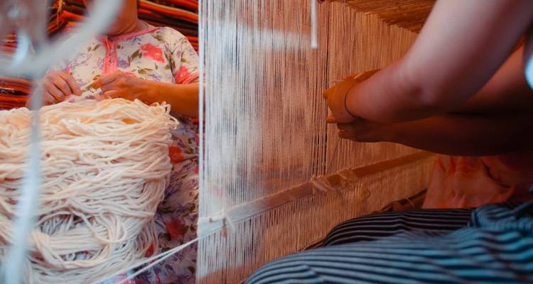 Nahaufnahme von Händen, die ein traditionelles Textil weben.