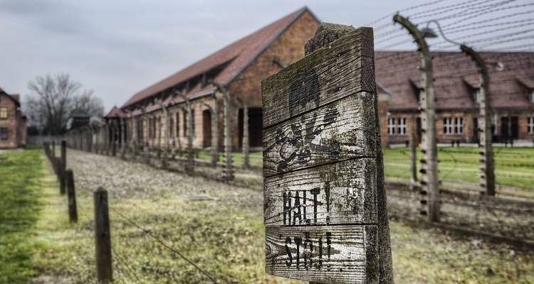 Letrero de advertencia desgastado y cerca de alambre de púas conducen hacia los barracones de ladrillo en el memorial de Auschwitz.