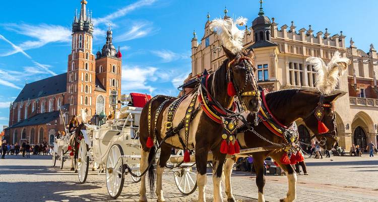 Elaborados carruajes tirados por caballos están de pie en la plaza principal de Cracovia junto a la Basílica de Santa María bajo cielos azules.