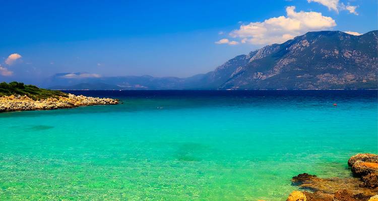 El mar turquesa vibrante se encuentra con las montañas escarpadas a lo lejos bajo un cielo de verano brillante en la costa turca.