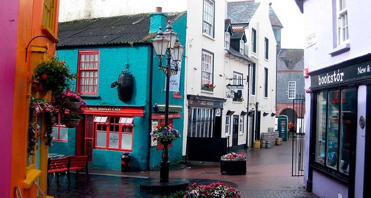 Charmante ruelle piétonne avec des devantures de magasins aux couleurs vives, des jardinières fleuries et des bancs à Kinsale.