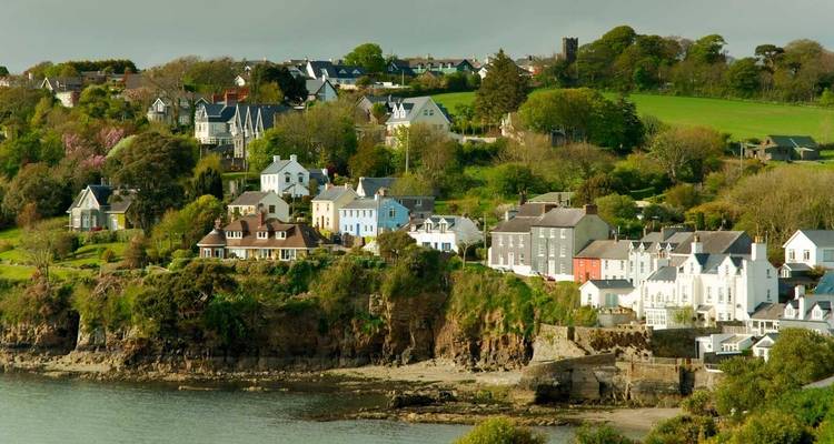 Maisons colorées regroupées sur une falaise verte au-dessus de la mer dans un village côtier irlandais pittoresque.