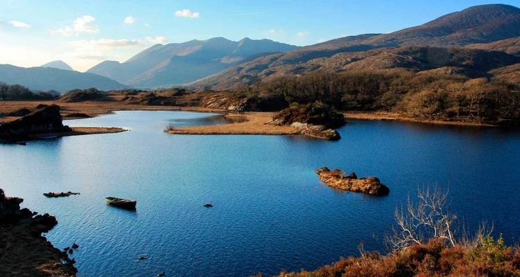 Un lac bleu bordé de petites îles se trouve sous des montagnes escarpées et un ciel clair.