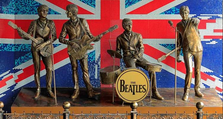 Des statues de bronze des Beatles en représentation se dressent devant une grande mosaïque d'Union Jack en arrière-plan.