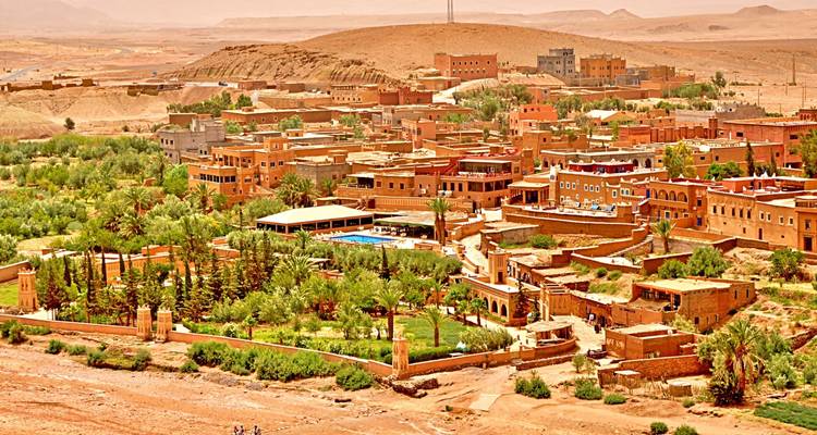 Panoramic view of an ochre desert settlement with lush palm gardens set against arid hills.