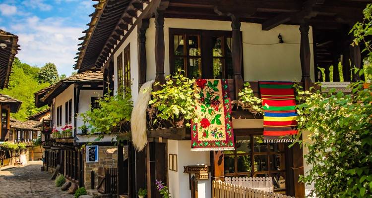 Ruelle pavée avec des maisons bulgares traditionnelles ornées de tapis tissés colorés et de fleurs.
