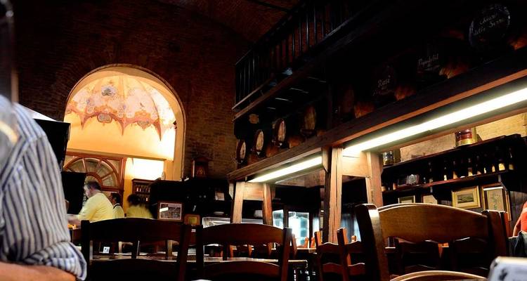 Interior cálidamente iluminado de una trattoria italiana rústica con barriles de madera, estantes de vino y comensales sentados en mesas de madera.