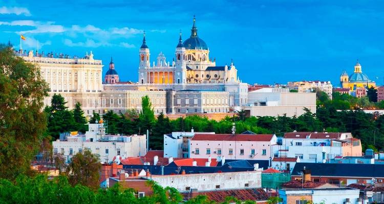 Panoramisch stadsbeeld van Madrid met de Almudena Kathedraal, het Koninklijk Paleis en omliggende daken onder een heldere blauwe hemel.