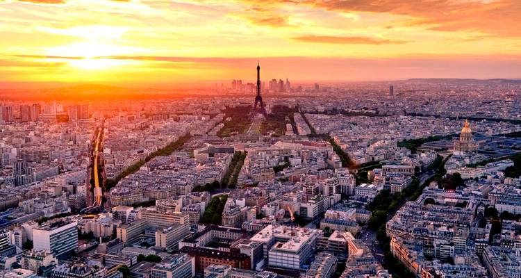 Una panorámica aérea amplia de París con la Torre Eiffel en el centro resplandeciendo bajo un cielo de atardecer naranja vívido.