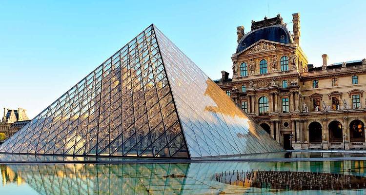 Pirámide de Cristal del Louvre reflejada en una piscina tranquila junto al palacio histórico al amanecer.